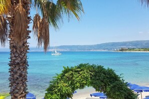 A beach with clear blue water, a sailboat, and a palm tree. - Residence Albatros (Briatico)