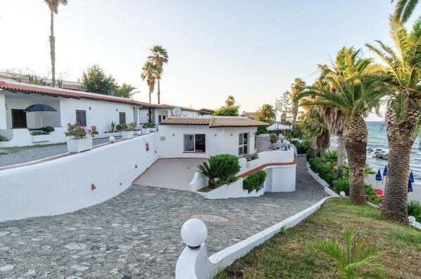 A coastal hotel with white buildings, a paved courtyard, and palm trees. - Residence Albatros (Briatico)
