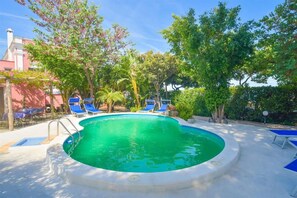 A swimming pool with blue lounge chairs, surrounded by trees and a building in the background. - Albergo Italia (Casamicciola Terme)