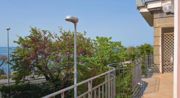 A balcony with a metal railing overlooking a body of water, surrounded by greenery and a clear sky.