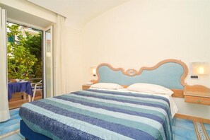 A hotel room with a large bed, a nightstand, a bedside table, and a view of the outdoors through a sliding glass door. - Albergo Italia (Casamicciola Terme)