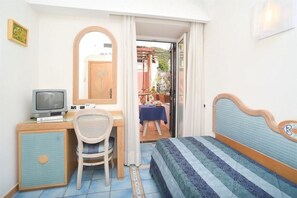 Un dormitorio con cama, escritorio con computadora, una silla y vista a un patio exterior.