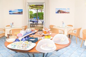 Un bufé de desayuno con diversas opciones de comida y bebidas, vista al jardín y mesas al aire libre.