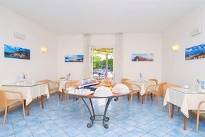 Un comedor con mesas y sillas, una mesa central de servicio y cuadros en las paredes.