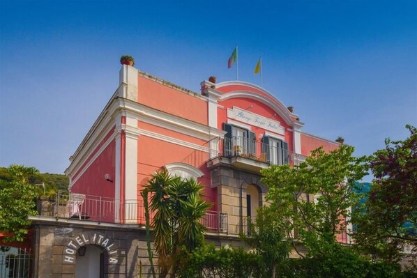 Un hotel de fachada roja, con un balcón y banderas en la parte superior.