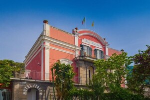 Un hotel con facciata rossa, un balcone e bandiere sulla sommità.
