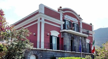 A building with a red facade, a balcony with a railing, and a flag.
