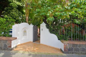 Una entrada tancada amb una porta decorativa blanca, un mur de pedra i un camí empelat que condueix a un edifici.