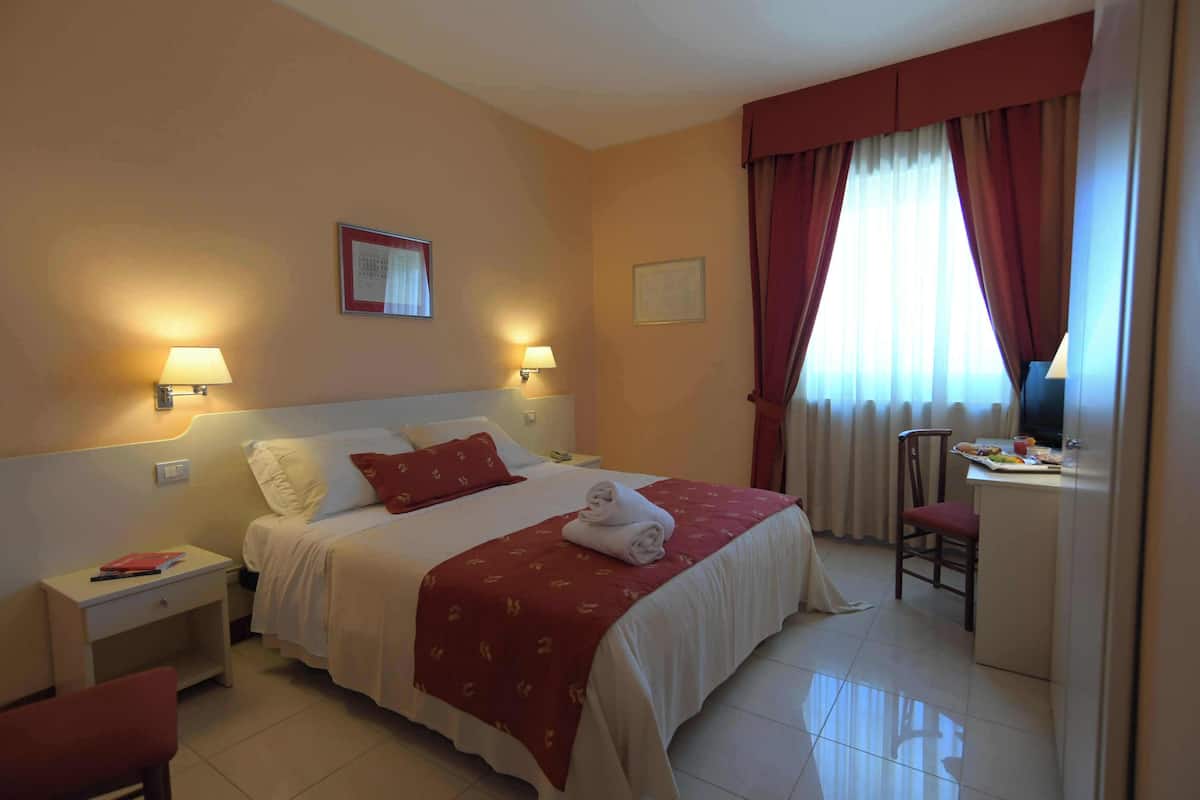 A hotel room with a bed, bedside tables, a desk, and a chair.