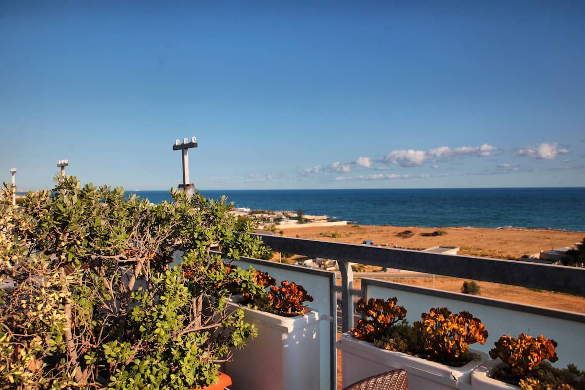 A seaside view with a balcony overlooking the ocean, a beach, and a lighthouse in the distance.