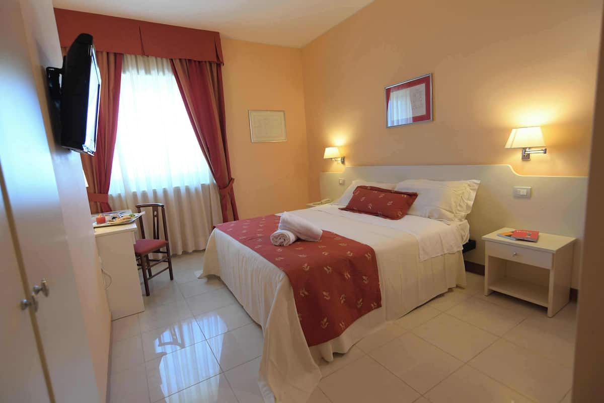 A hotel room with a bed, bedside lamps, a desk, a chair, and a television.