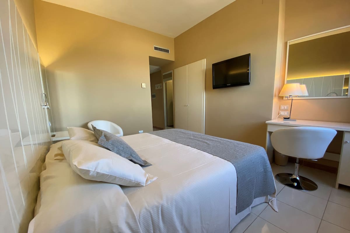 A hotel room with a bed, a desk, a chair, a TV, and a lamp.