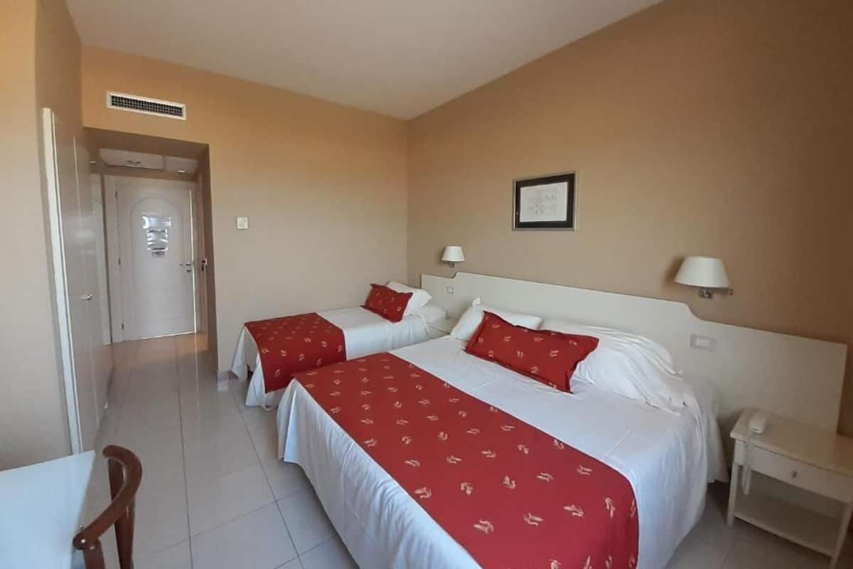 A hotel room with two beds, a desk, a chair, a phone, and a picture on the wall.