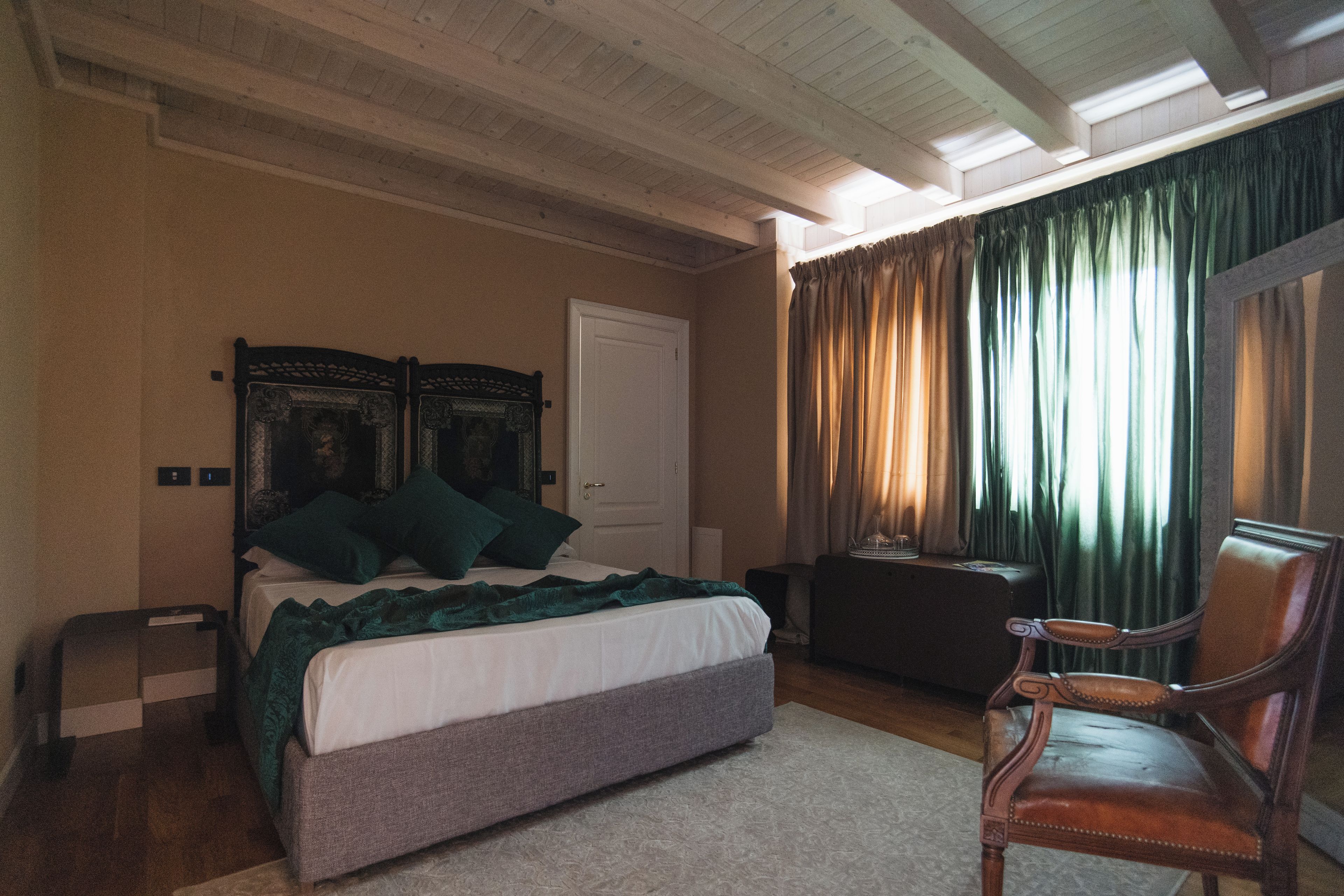 A bedroom with a bed, a chair, a desk, and a window with curtains.