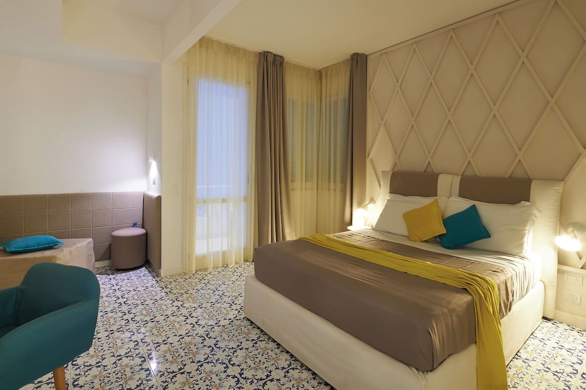 A hotel room with a bed, a chair, a small table, and a window with curtains.