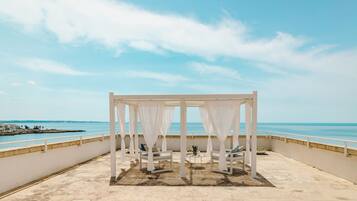 A white outdoor seating area with a view of the sea.