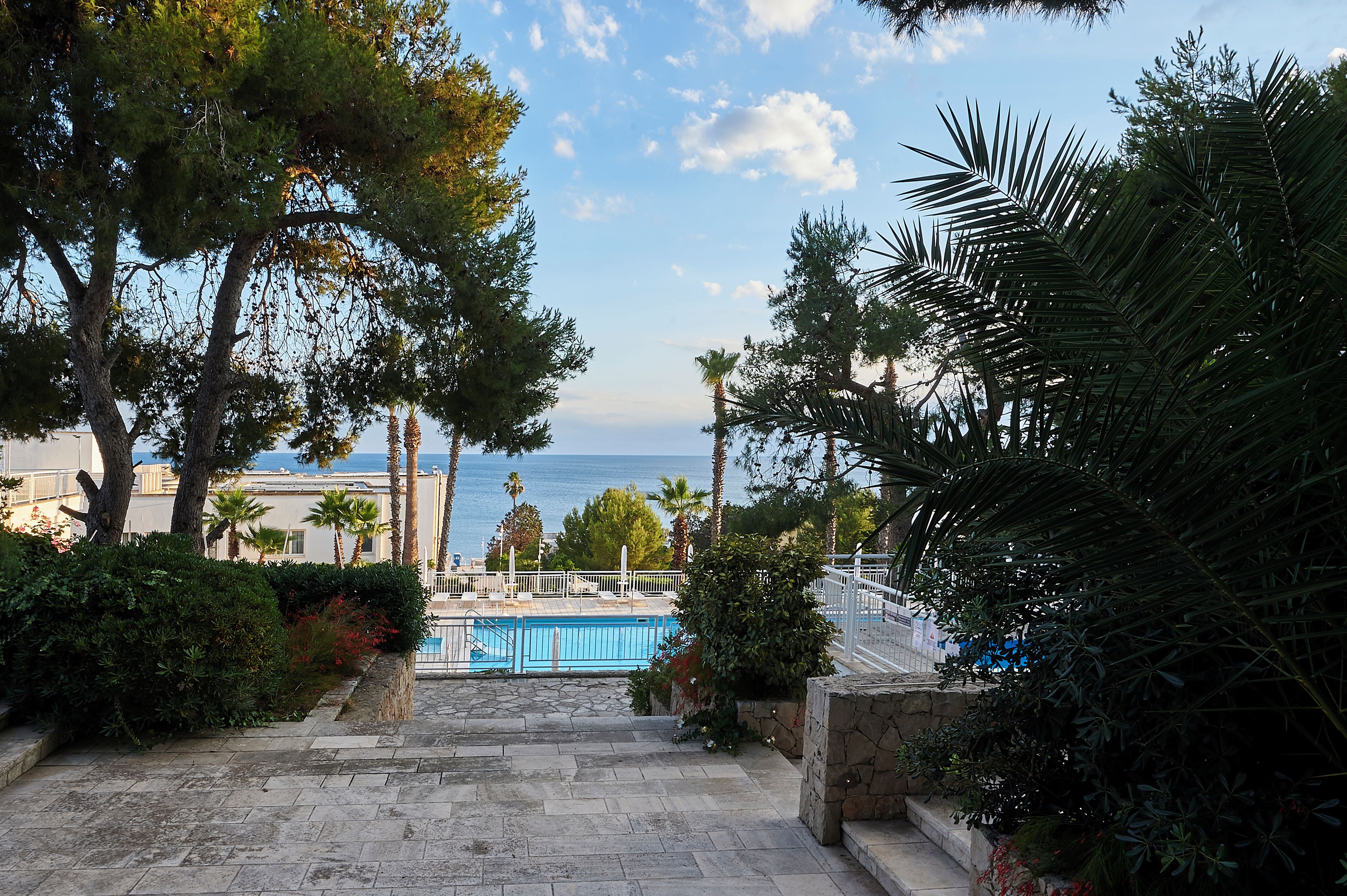A pool area with steps leading down to the water, surrounded by trees and a view of the sea.