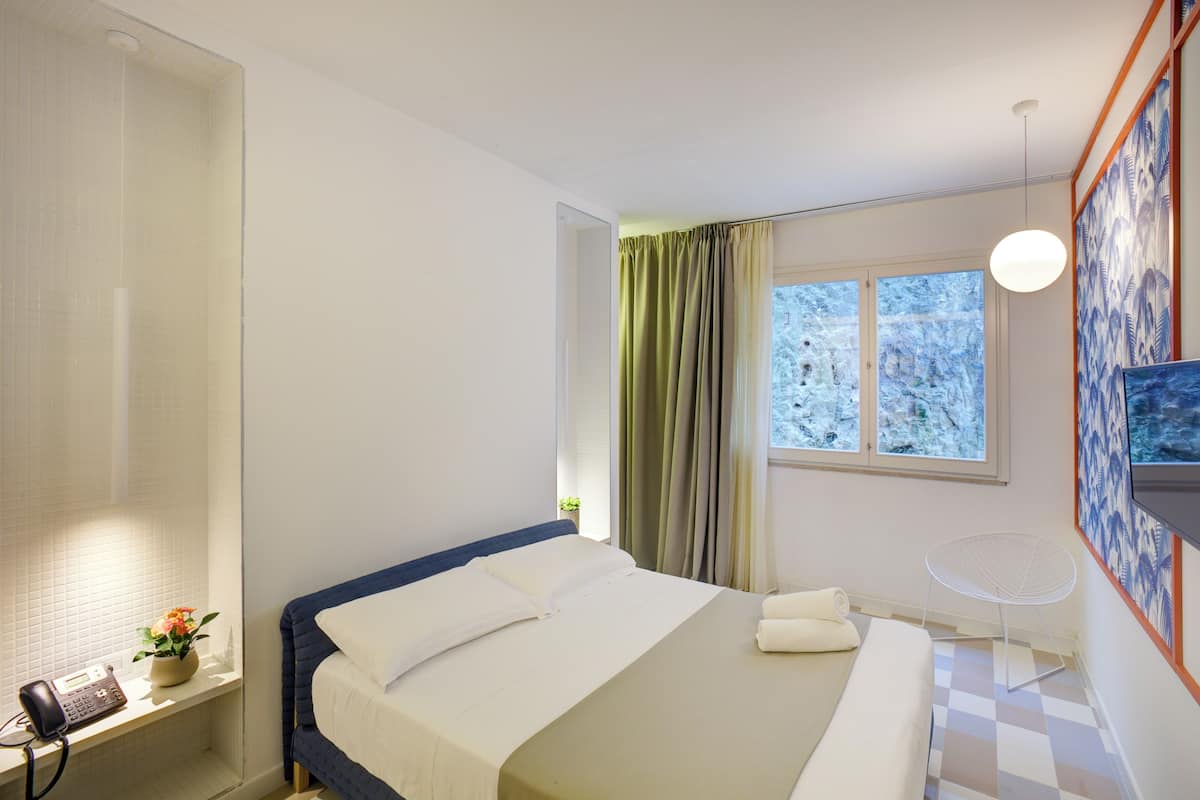 Ein Hotelzimmer mit Bett, Schreibtisch mit Telefon, Stuhl, Fernseher und einem Fenster mit Vorhängen.