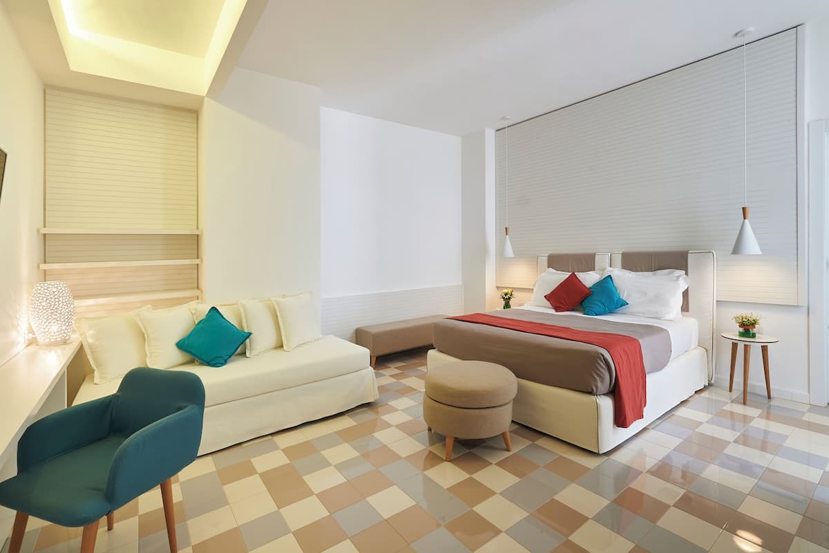 Ein modernes Hotelzimmer mit einem Bett, einem Schlafsofa, einem Sessel und einem kleinen Tisch.