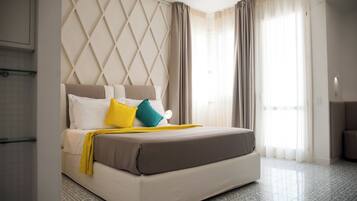 Una camera d'albergo con un letto grande, una testata imbottita con motivo a diamante e vista all'esterno attraverso ampie finestre.