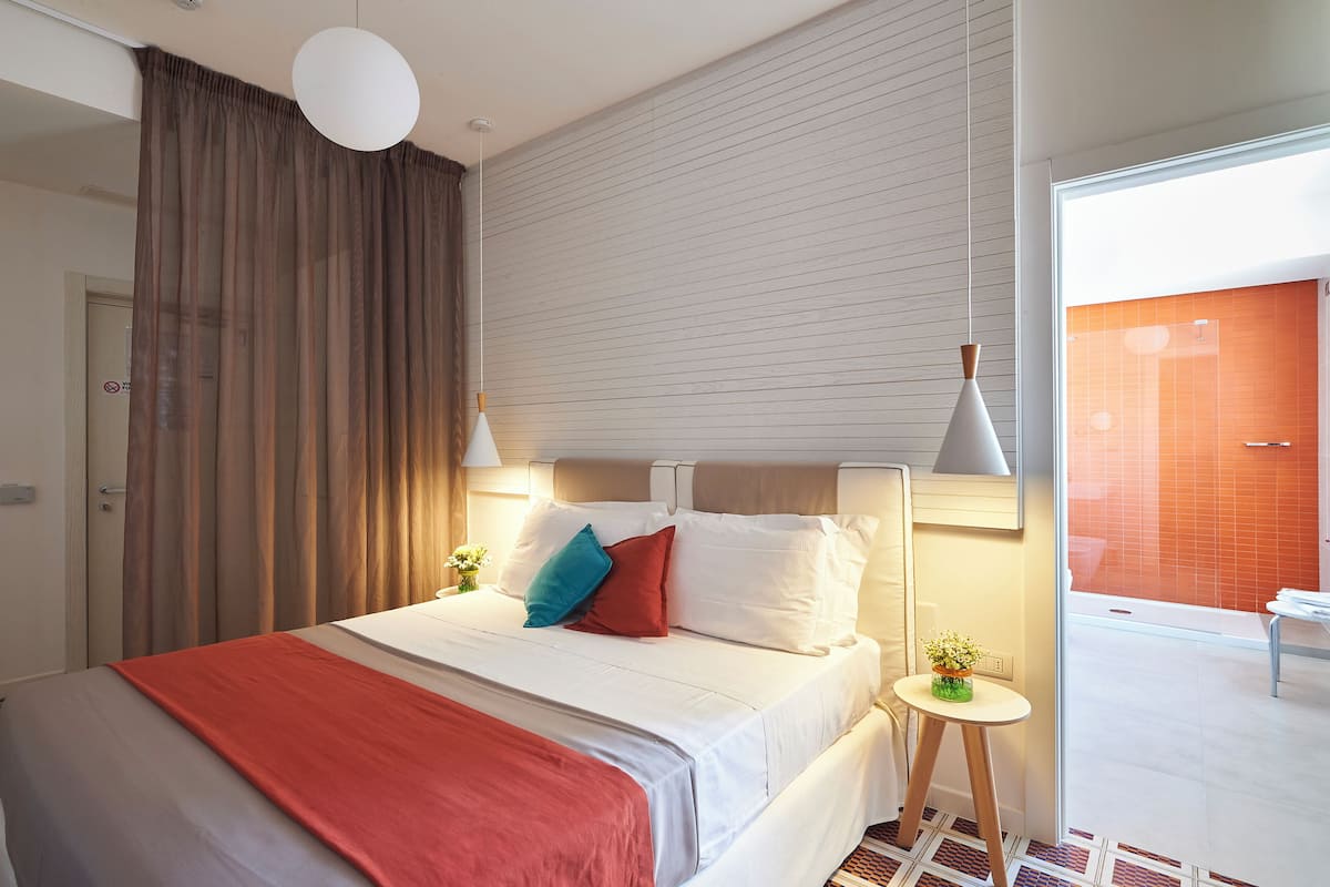 Ein modernes Hotelzimmer mit einem großen Bett, einem kleinen Tisch mit einer Pflanze und Blick ins Badezimmer.