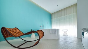 A modern bathroom with a turquoise wall, a white bathtub, and a rocking chair. - Grand Hotel Riviera CDS Hotels (Nardò)