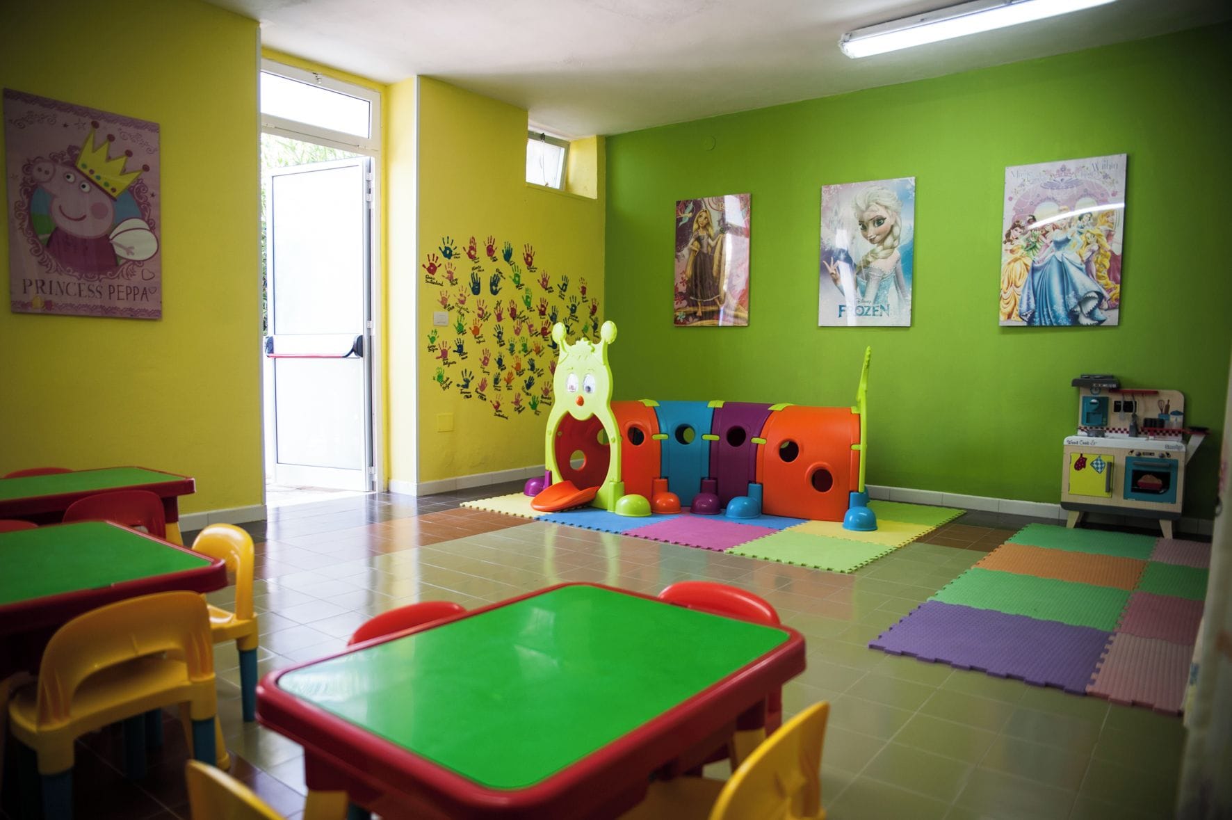 A brightly colored children's playroom with tables, chairs, and educational posters on the walls.