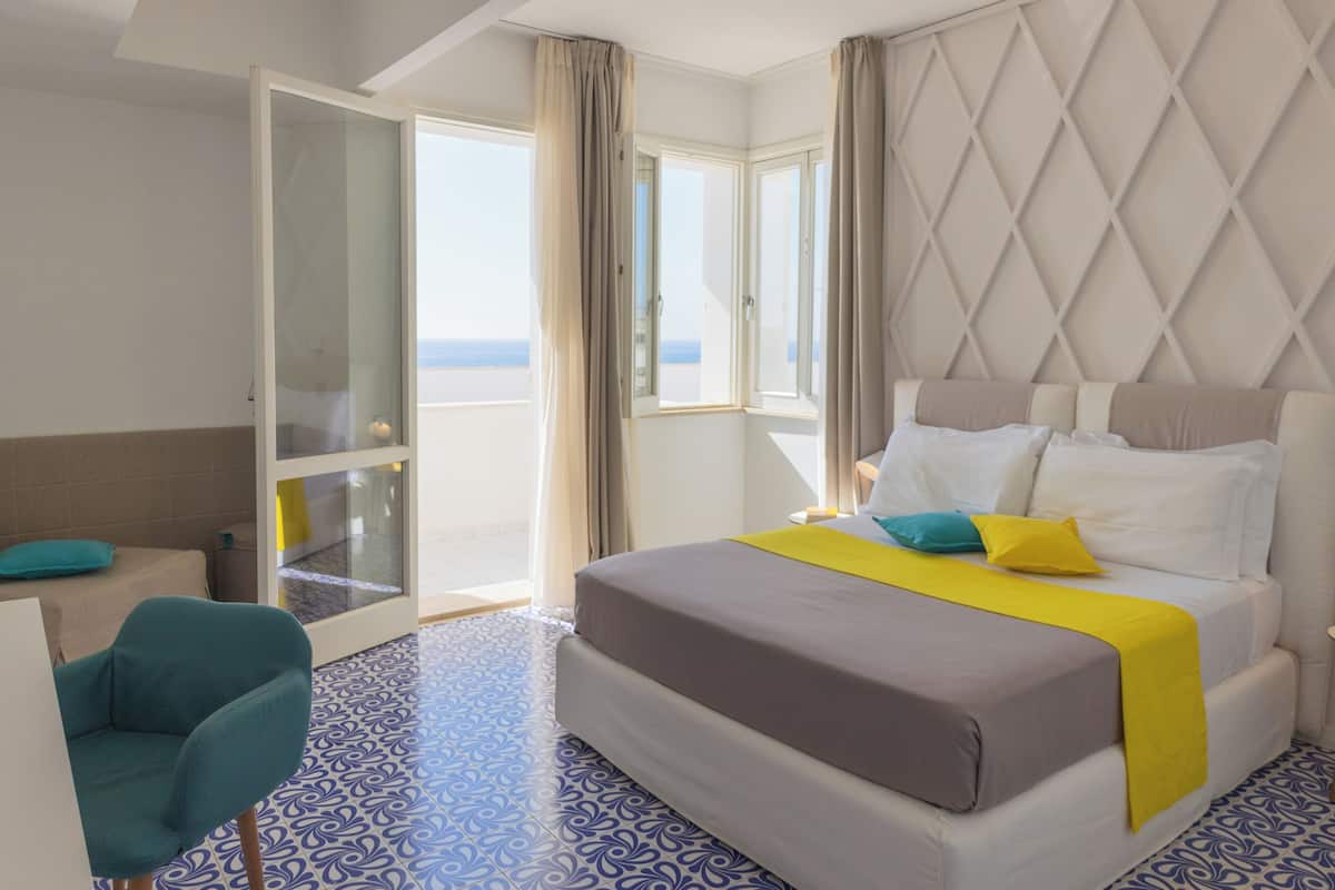 Ein Hotelzimmer mit Bett, Sessel, Schreibtisch und Meerblick durch große Fenster.