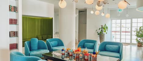 A modern living room with teal armchairs, a glass coffee table, and a green accent wall.