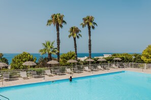 A swimming pool with lounge chairs and umbrellas, surrounded by palm trees and a view of the sea. - Grand Hotel Riviera CDS Hotels (Nardò)