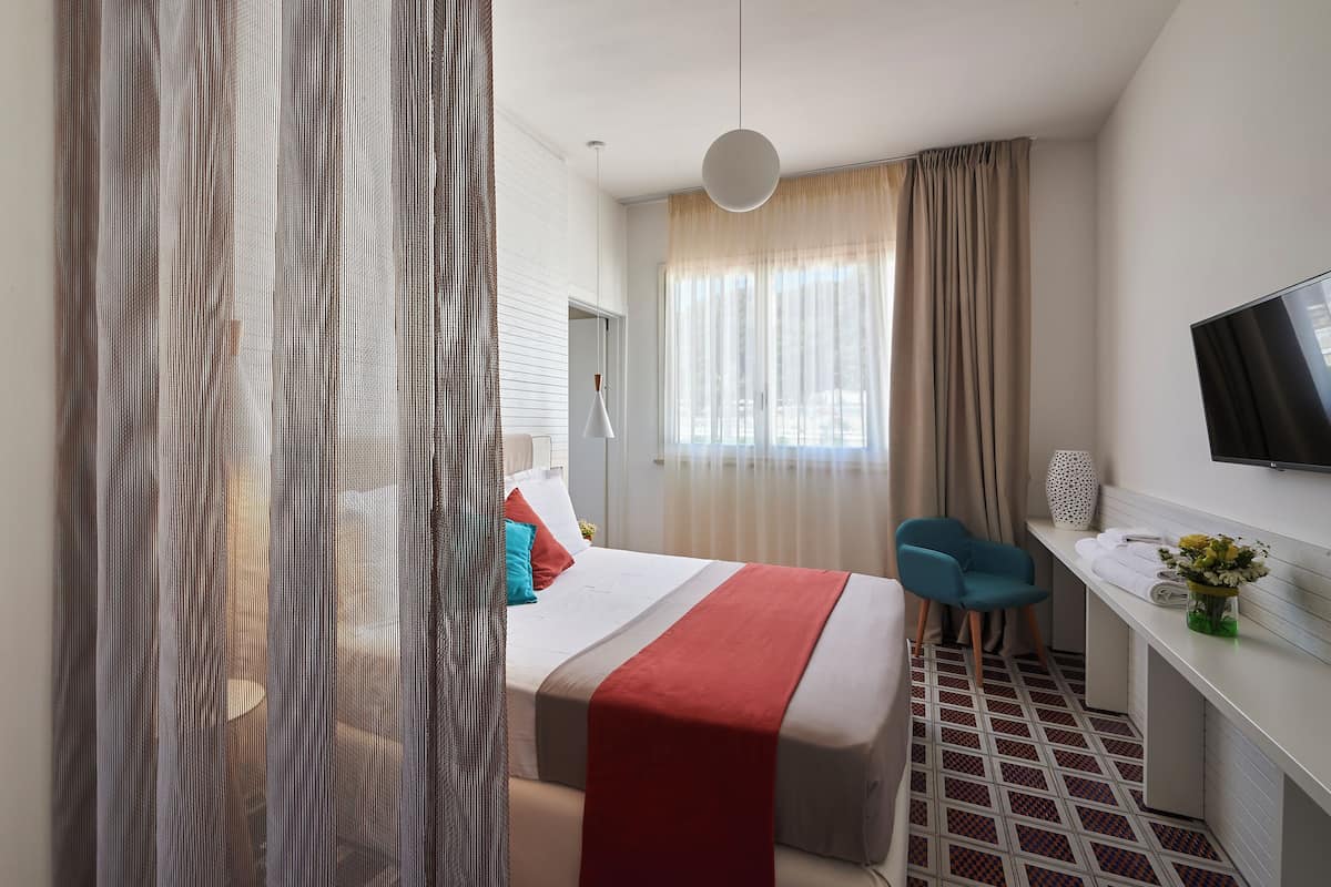 Ein Hotelzimmer mit Bett, Schreibtisch, Fernseher und einem Fenster mit Vorhängen.