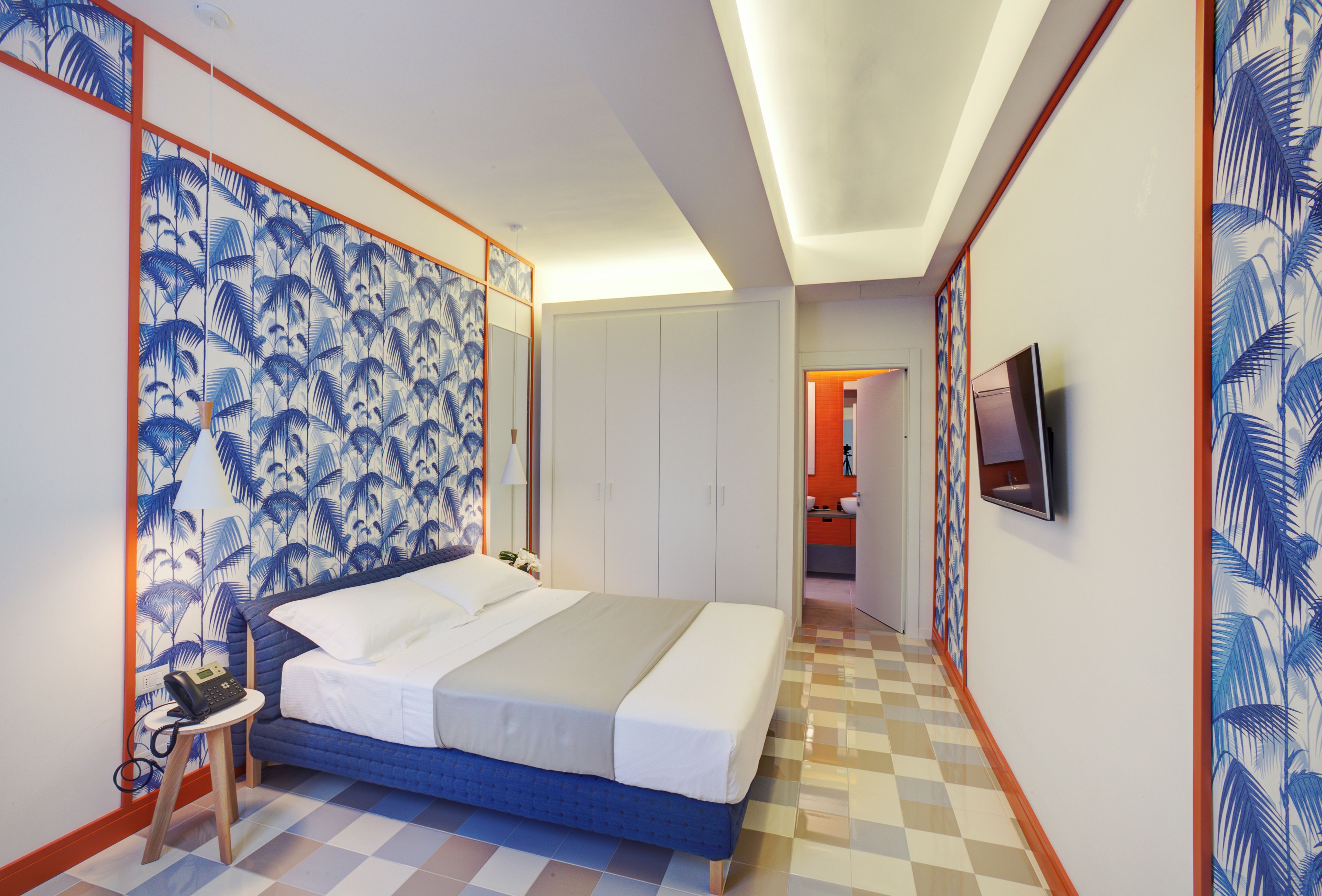 A hotel room with a bed, a desk with a telephone, and a television on the wall.