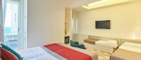 Habitación de hotel con una cama grande, una cama más pequeña, un escritorio y una silla. Hay una ventana con cortinas, un cuadro en la pared y vistas al mar.
