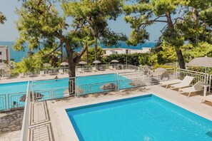 A pool area with lounge chairs and umbrellas, surrounded by trees and overlooking a body of water. - Grand Hotel Riviera CDS Hotels (Nardò)