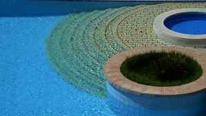 Une piscine à l’eau d’un bleu limpide, un parterre circulaire en briques planté d’herbe et un bord carrelé.