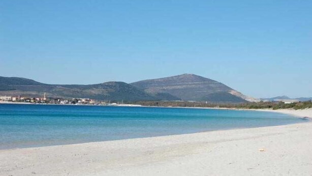 Une plage avec une eau d’un bleu limpide, un rivage sablonneux et une montagne en arrière-plan.