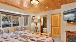 Un dormitorio con una cama grande, techo de madera, televisor y vistas al exterior.
