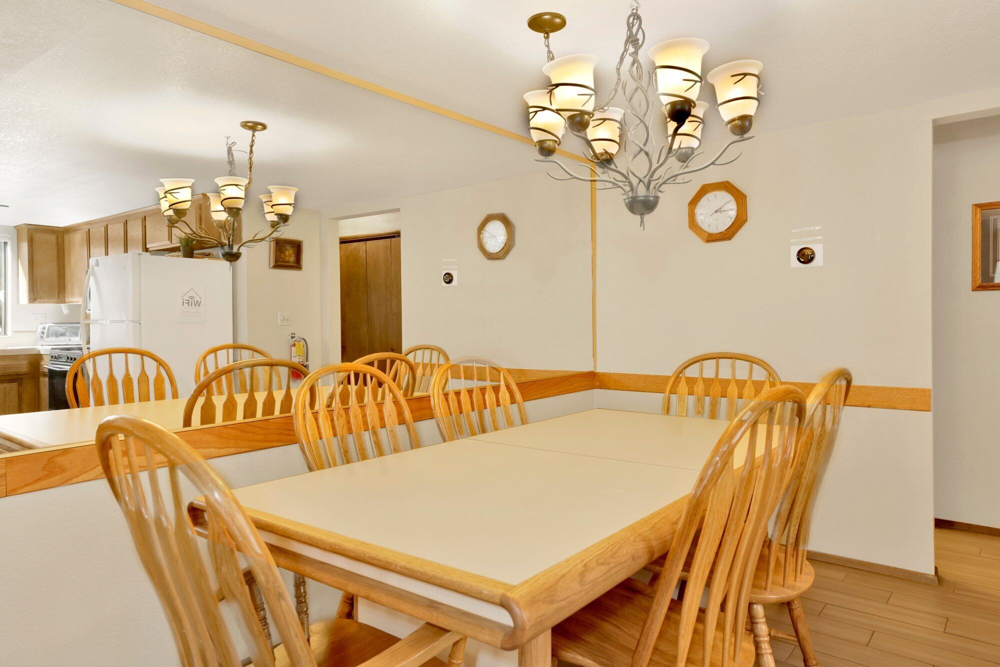 Un comedor con una mesa grande y sillas de madera, una araña y un reloj en la pared.