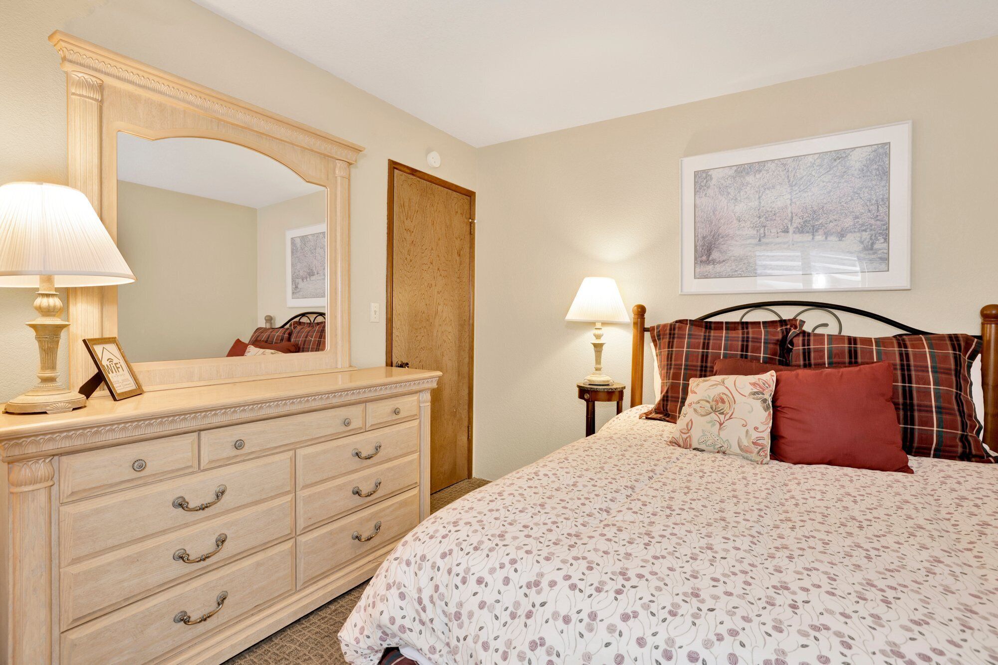A bedroom with a bed, a dresser, a mirror, a nightstand, and a framed picture on the wall.