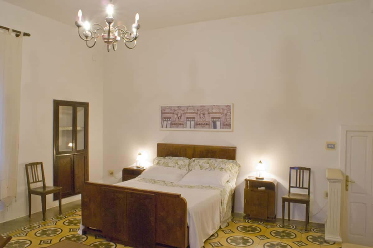 Un dormitorio con una cama de madera, dos mesitas de noche, una araña, un espejo y una puerta.