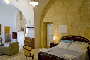 Een slaapkamer met een bed, een stoel, een nachtkastje en een lamp.