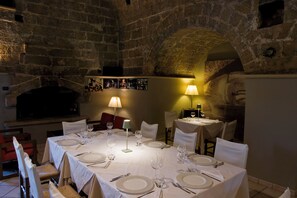 Un espace repas aux murs de pierre, nappes blanches et ambiance tamisée à la lumière des bougies.