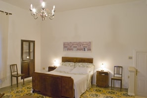 Un dormitorio con una cama de madera, dos mesitas de noche, una araña, un espejo y una puerta.