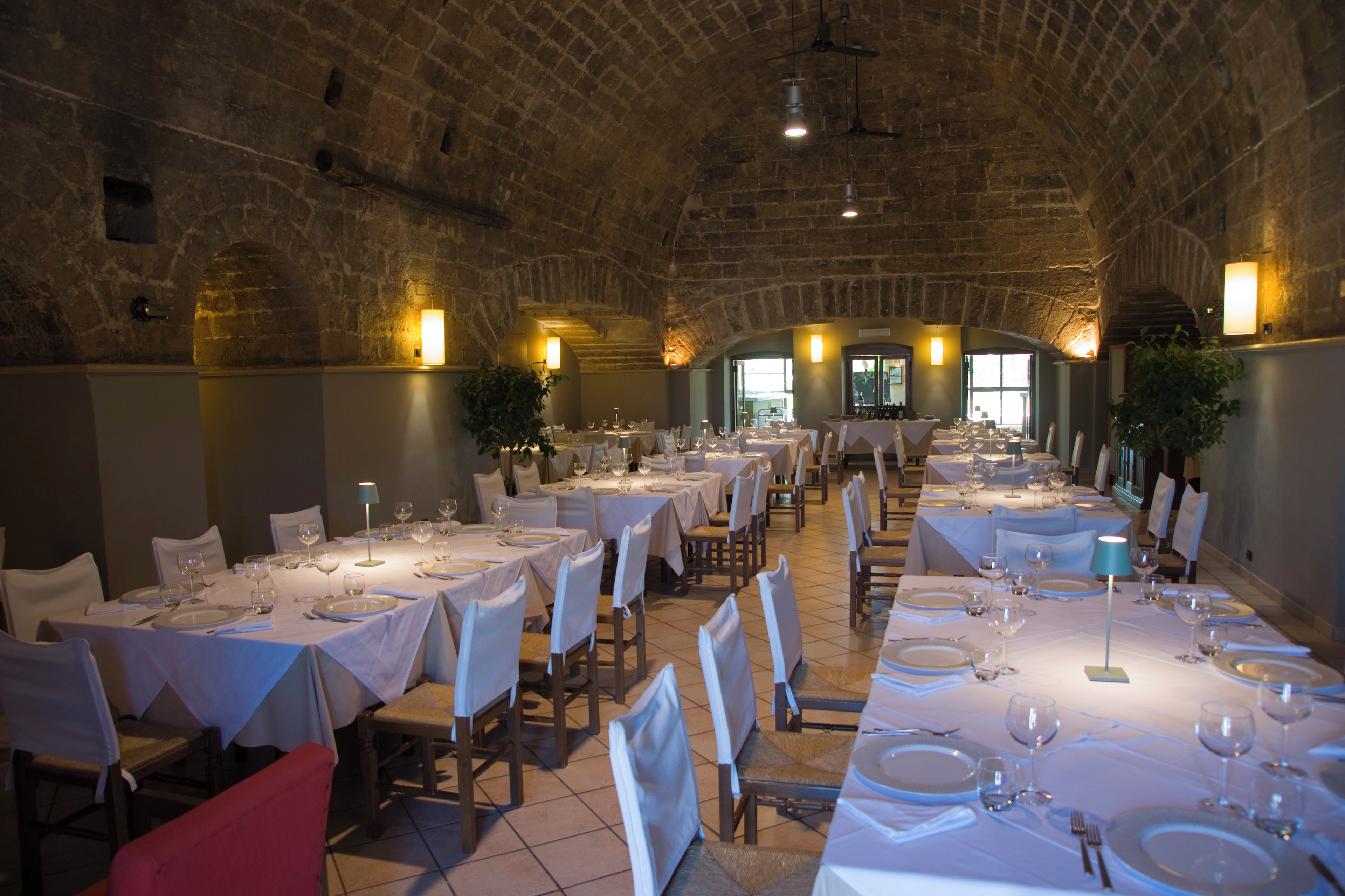 Ein Restaurant mit mehreren Esstischen, einem Steingewölbe und natürlichem Licht durch Fenster.