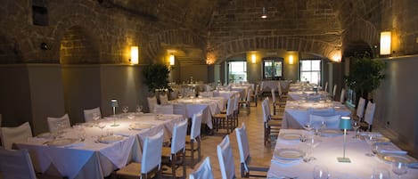 Un restaurante con varias mesas dispuestas para comer, que presenta un techo de piedra e iluminación natural gracias a las ventanas.