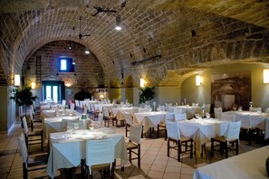 Een restaurant met meerdere tafels klaar voor dineren, met een bakstenen plafond en stenen muren.