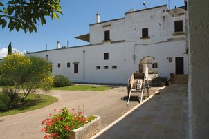 Un patio con un edificio blanco, un carro de madera y una cama de flores.