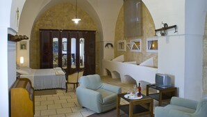 A living room with a bed, two armchairs, a small table, a television, and a large arched doorway. - Masseria Zanzara (Presicce-Acquarica)