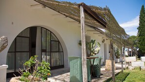 A building with a white exterior, large arched windows, and a covered patio area with outdoor furniture. - Masseria Zanzara (Presicce-Acquarica)