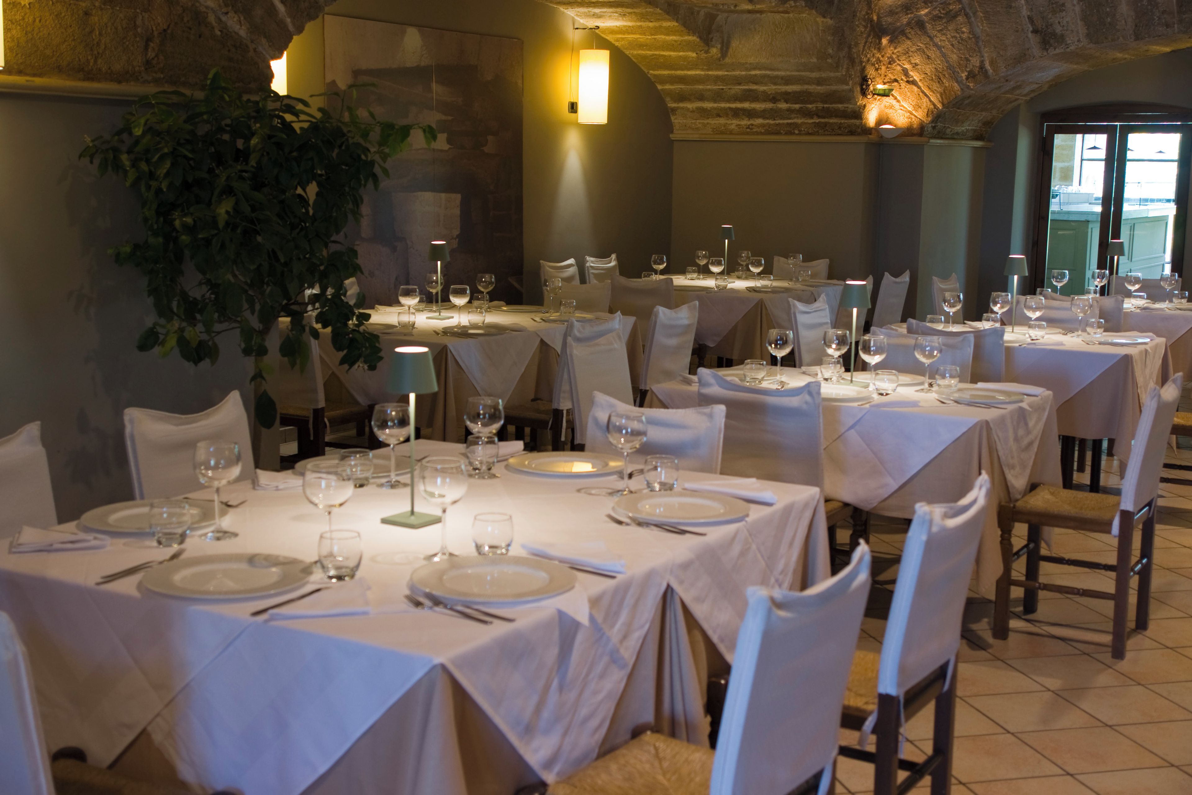 A restaurant with multiple tables set for dining, each with white tablecloths, chairs, and wine glasses.